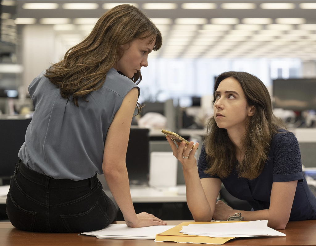 scene from "She Said," two women listening to cell phone call on speaker in a newsroom. Present Day.